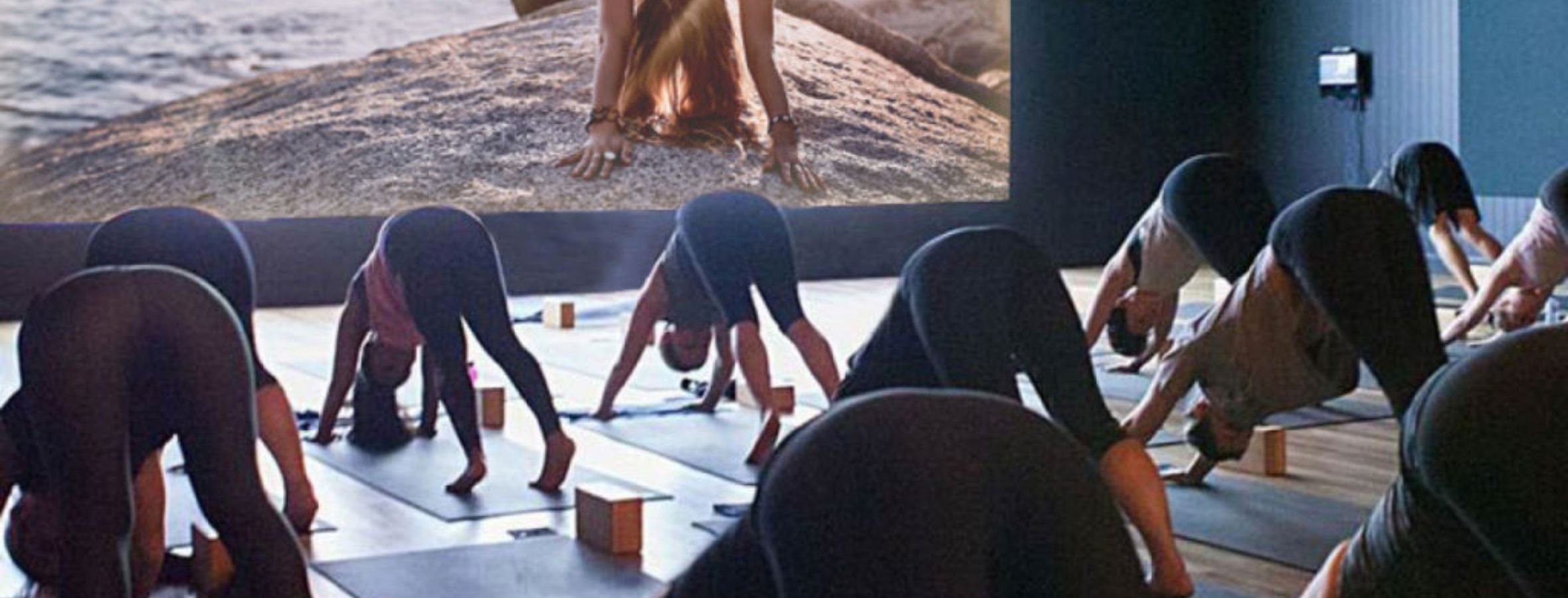 A virtual Yoga class in front of a large video wall displaying the class content