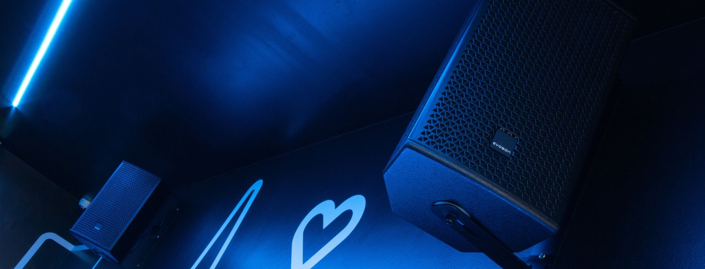 Two wall mounted cabinet loudspeakers in a blue lit room as part of an AV installation