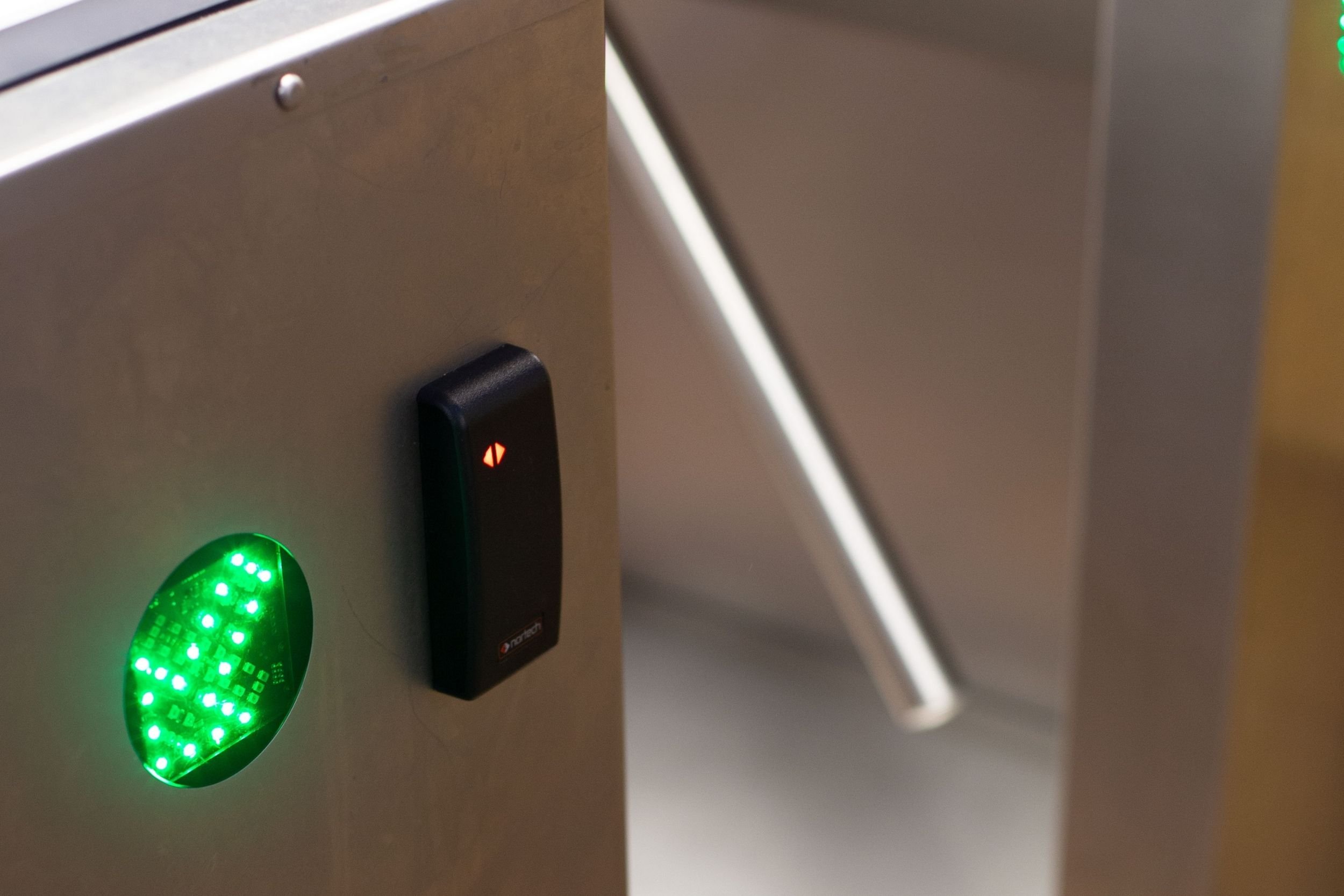 An access control card reader next to a green LED arrow light on a tripod turnstile