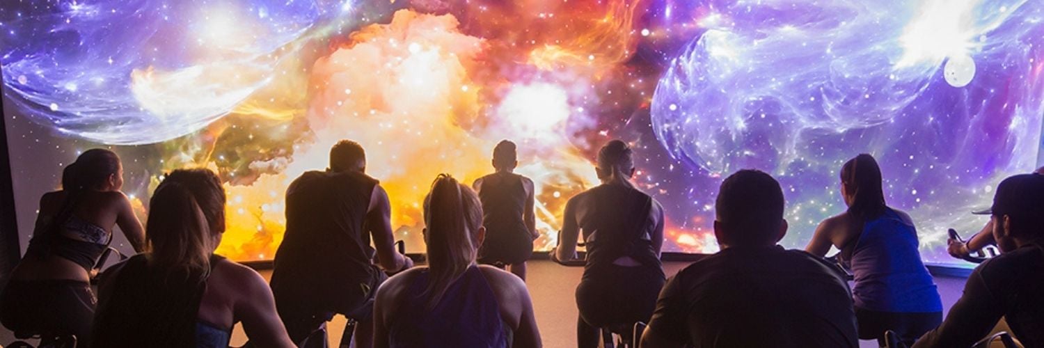 A spin class in front of a virtual cycling video wall showing a space scape